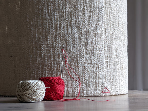 close up image of two spools of pearl cotton thread (one red, one ecru) in front of a textured boucle lamp shade with a red triangle stitch detail