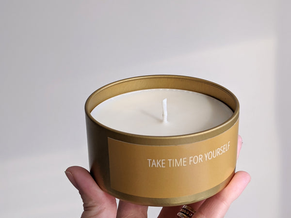 Hand holding a candle tin that reads 'Take Time for Yourself'