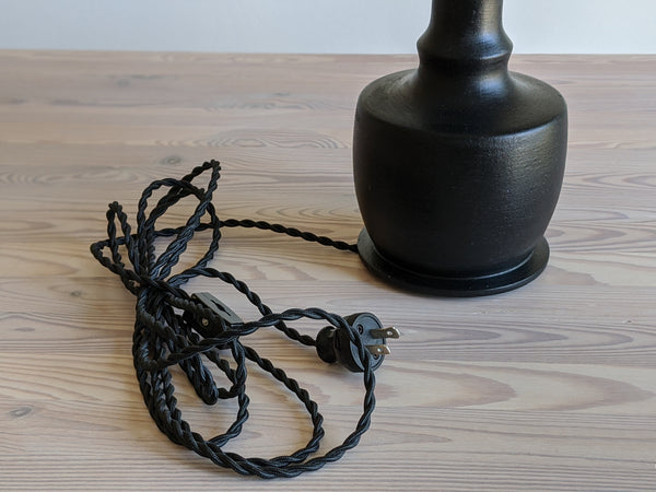 Close up of black twisted cord with vintage style plug on black table lamp.