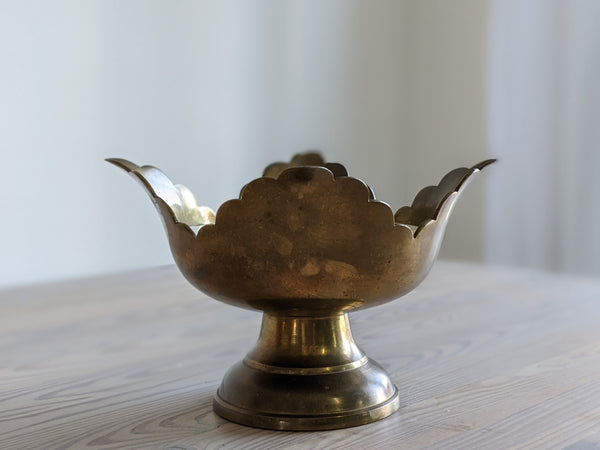 vintage scalloped brass candle sitting on a light wood table in the sun